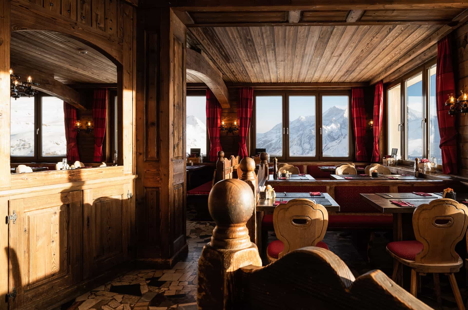 Rustic wooden restaurant interior with views of snow-covered mountains through large windows.