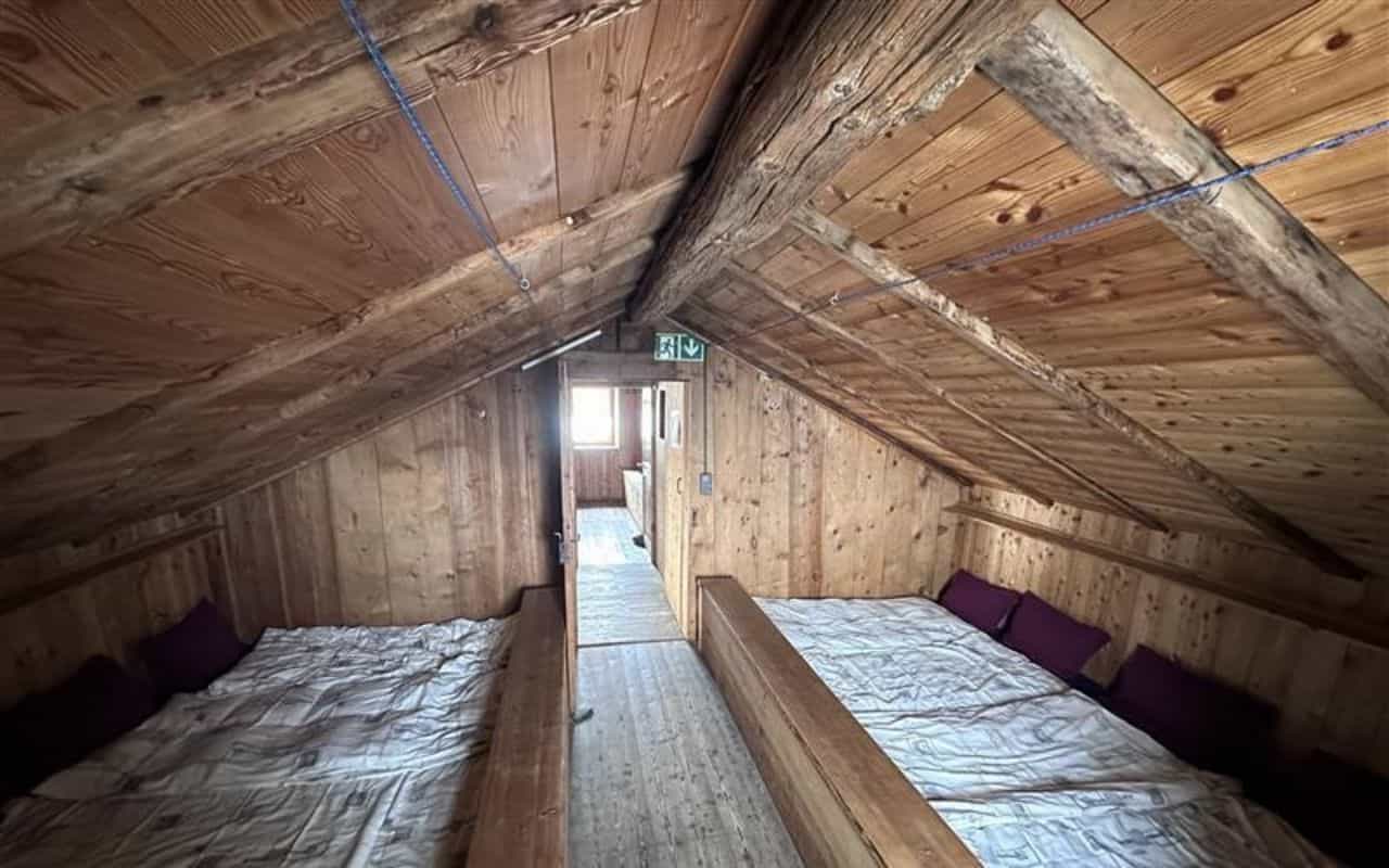 Attic sleeping area with wooden walls and ceiling, beds with white bedding, and green exit sign.