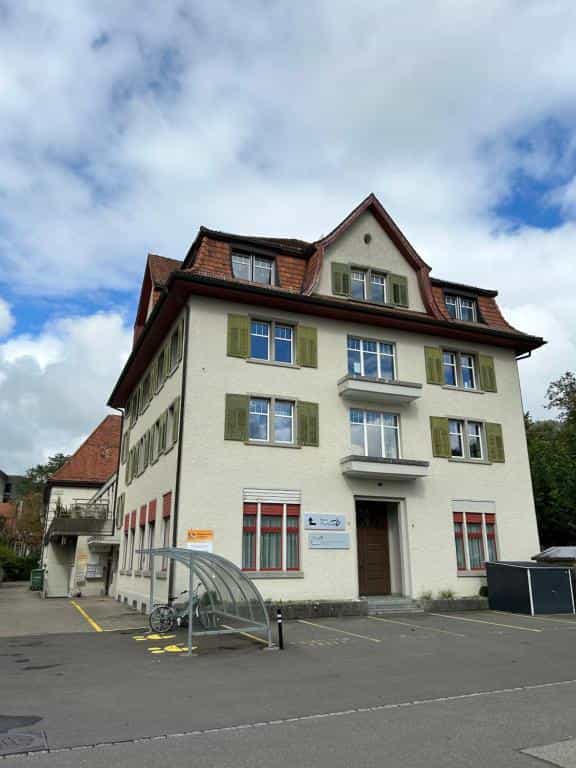 Cream-colored building with red roof and green shutters, bicycle rack in front, Hotel Thurpark setting.