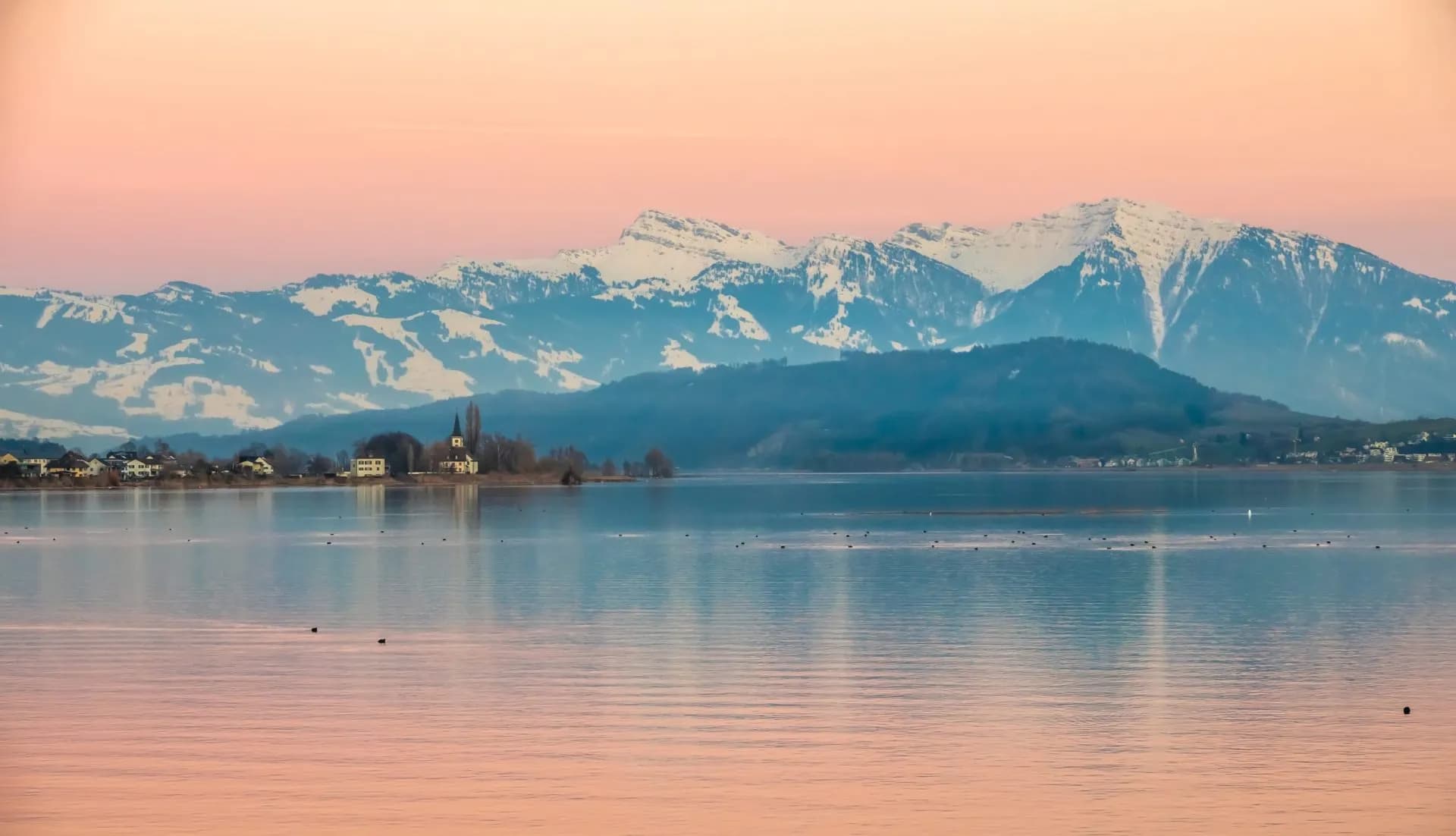 Gorgeous sunrise on Lake Zurich with snow-capped mountains and village shoreline