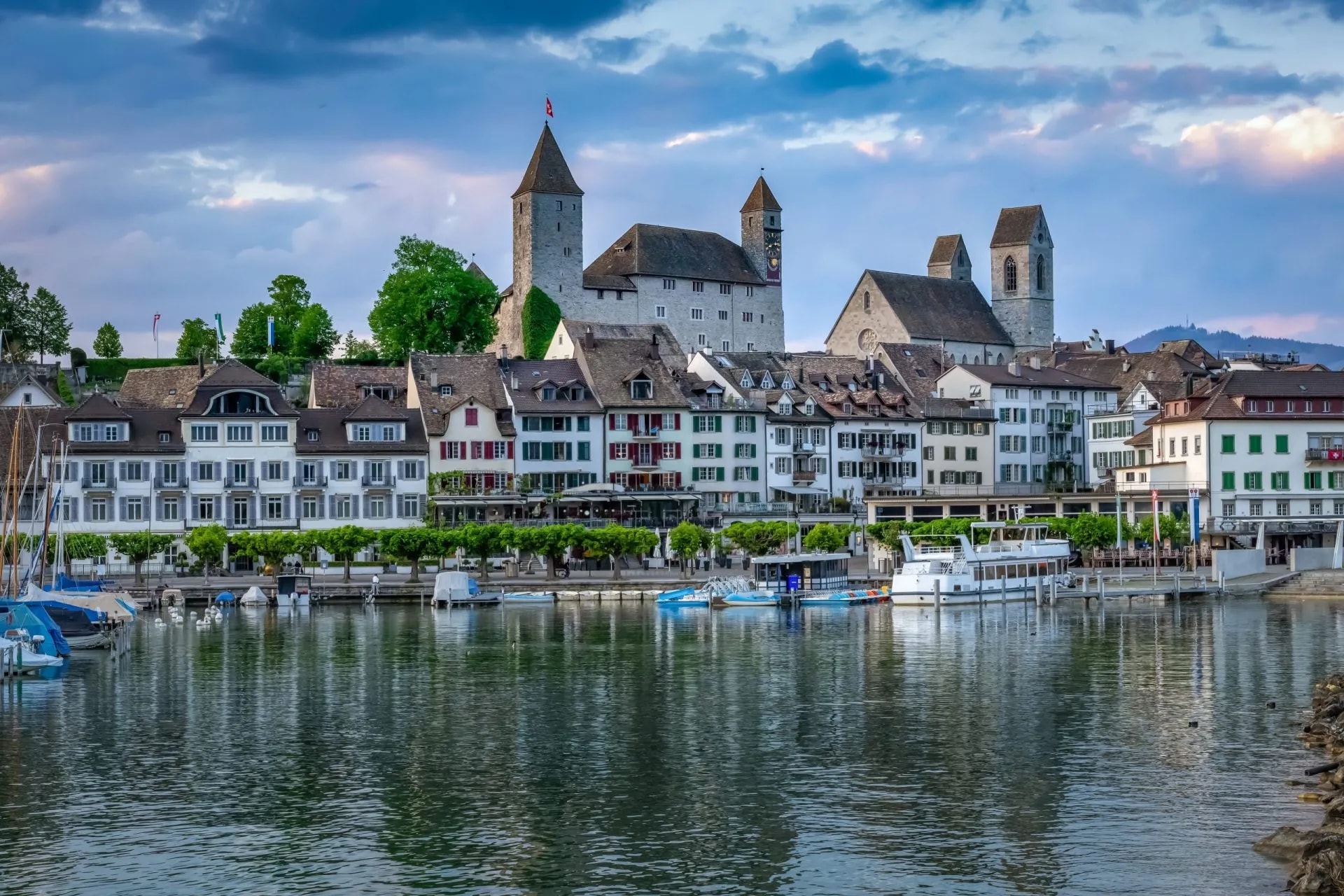 Waterfront town with historic buildings, castle, and boats docked on the water in Switzerland.