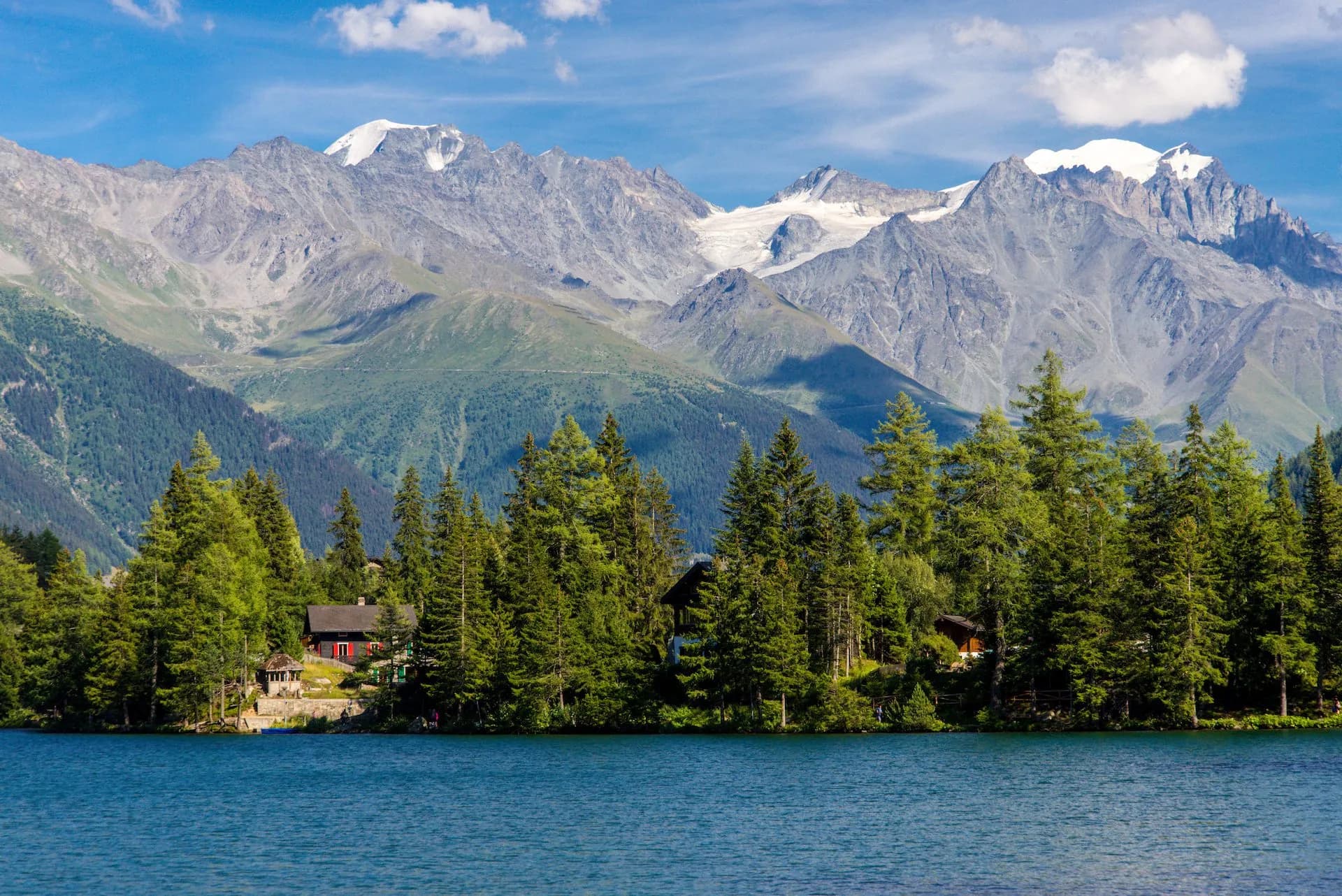 Alpine mountain lake Champex Lac with snow-capped peaks, pine trees, and lakeside cabins.