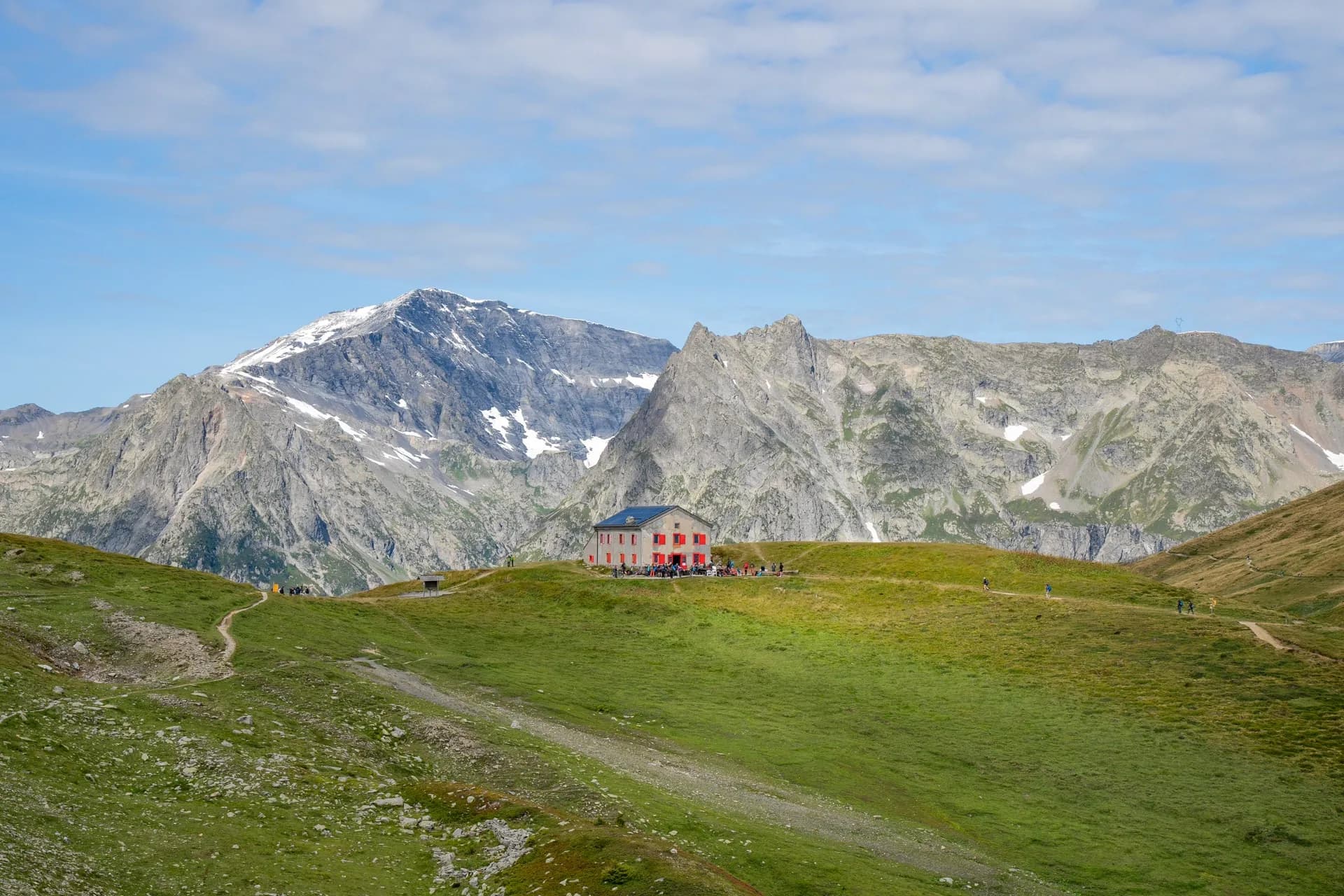The Hut at Col de Balme with hikers on green alpine slopes and snowy mountains.