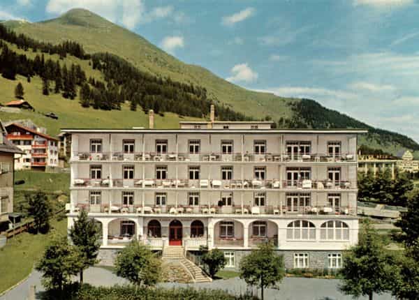 Edelweiss Hotel Davos with balconies set against a large green mountain under a blue sky.