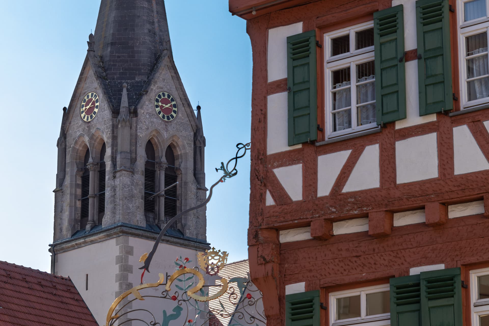 Church tower with clocks next to half-timbered building with green shutters in Münsingen.