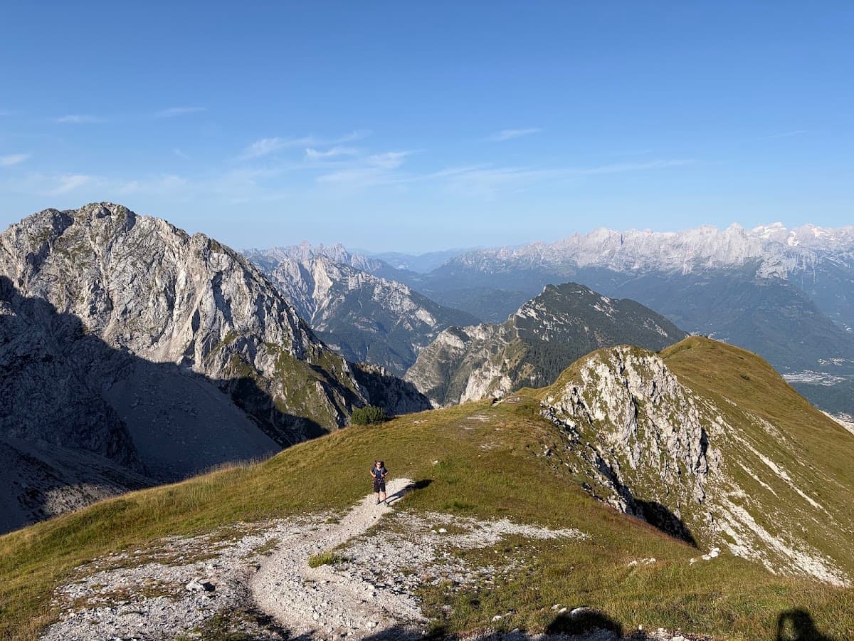 Hiker on a dirt trail amidst rugged alpine mountain peaks under a clear blue sky