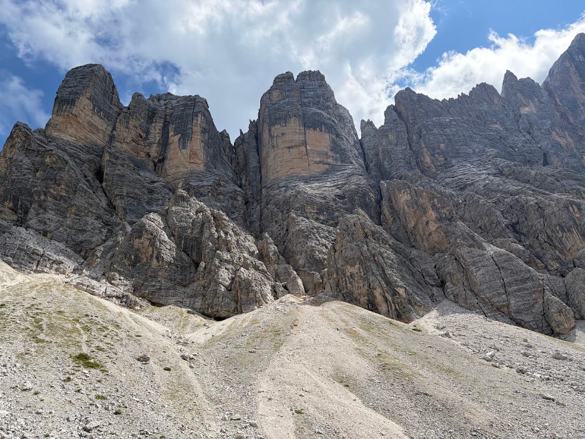 Rugged mountain peaks with rocky cliffs and a steep scree slope beneath a cloudy blue sky