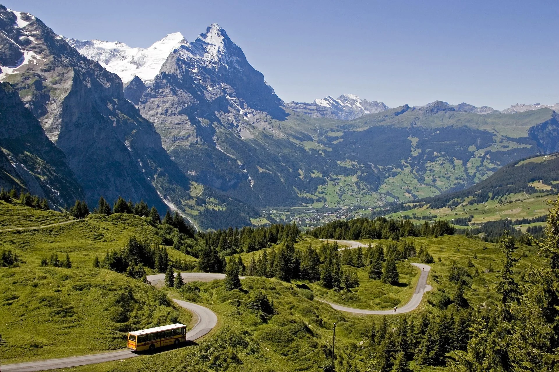 Yellow bus driving on winding mountain road near Grosse Scheidegg toward Grindelwald.